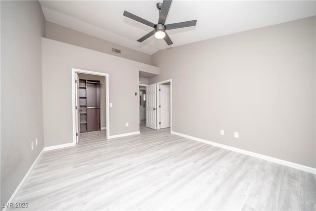 unfurnished bedroom featuring light wood-style floors, baseboards, a spacious closet, vaulted ceiling, and ceiling fan