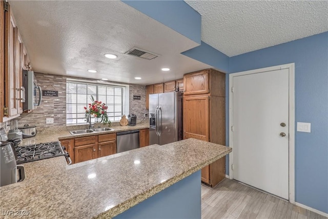 6408 Deadwood Rd, Las Vegas, NV 89108 - kitchen featuring appliances with stainless steel finishes, a sink, a textured ceiling, brown cabinets, and light wood-style flooring