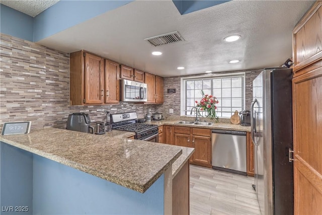 6408 Deadwood Rd, Las Vegas, NV 89108 - kitchen featuring stainless steel appliances, a sink, a peninsula, brown cabinets, and a textured ceiling