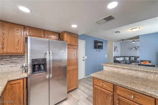 6408 Deadwood Rd, Las Vegas, NV 89108 - kitchen with stainless steel fridge, brown cabinetry, light wood-style floors, tasteful backsplash, and a textured ceiling