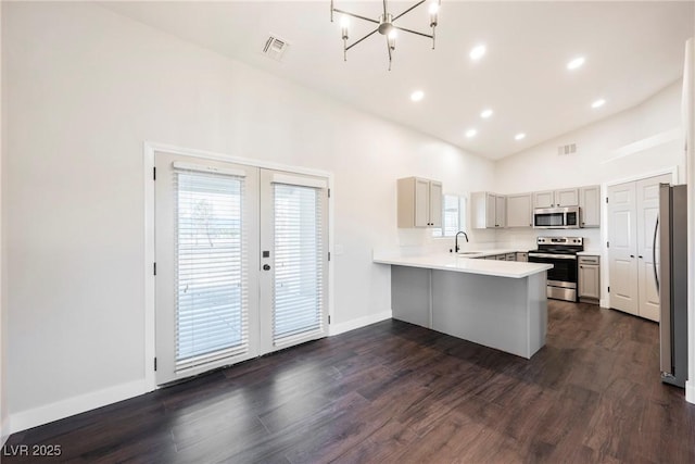 kitchen with stainless steel appliances, a peninsula, a sink, dark wood-type flooring, and vaulted ceiling