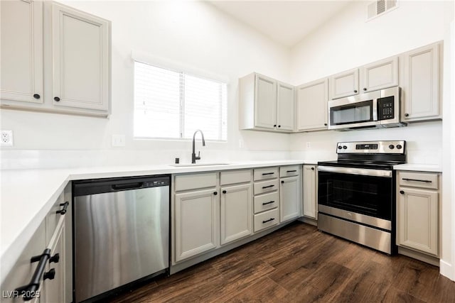 kitchen featuring appliances with stainless steel finishes, a sink, dark wood finished floors, and light countertops