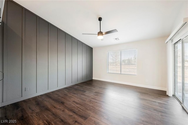 unfurnished room with dark wood-style flooring, a ceiling fan, and baseboards