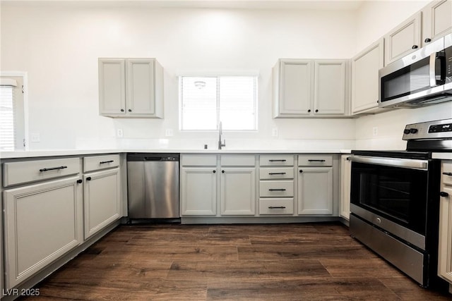 kitchen with appliances with stainless steel finishes, a sink, gray cabinetry, light countertops, and dark wood finished floors