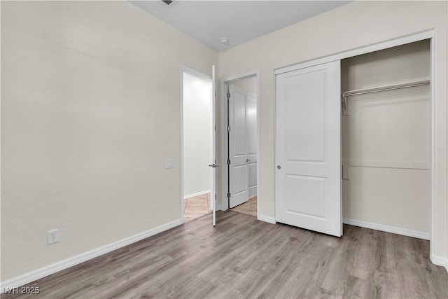 unfurnished bedroom featuring wood finished floors, a closet, and baseboards