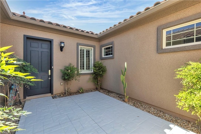 property entrance with a patio area, stucco siding, and a tile roof
