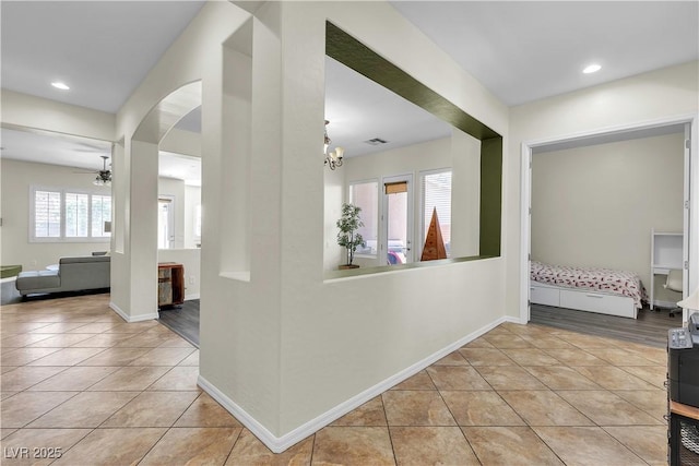 hallway featuring light tile patterned floors, arched walkways, a chandelier, recessed lighting, and baseboards