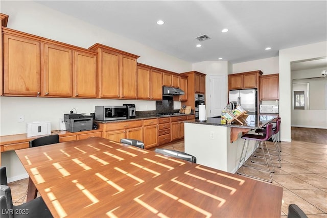 kitchen featuring appliances with stainless steel finishes, under cabinet range hood, light tile patterned floors, a kitchen breakfast bar, and a kitchen island with sink