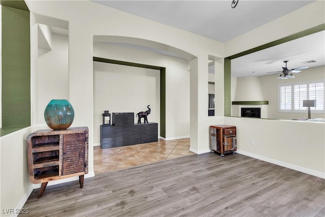 interior space featuring wood finished floors, a large fireplace, ceiling fan, and baseboards