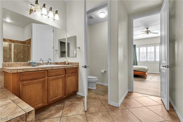 ensuite bathroom featuring toilet, a shower stall, ceiling fan, and baseboards