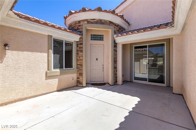 property entrance with stucco siding, a patio area, stone siding, and a tile roof
