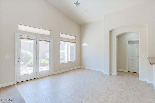 empty room with high vaulted ceiling, arched walkways, light tile patterned floors, and baseboards
