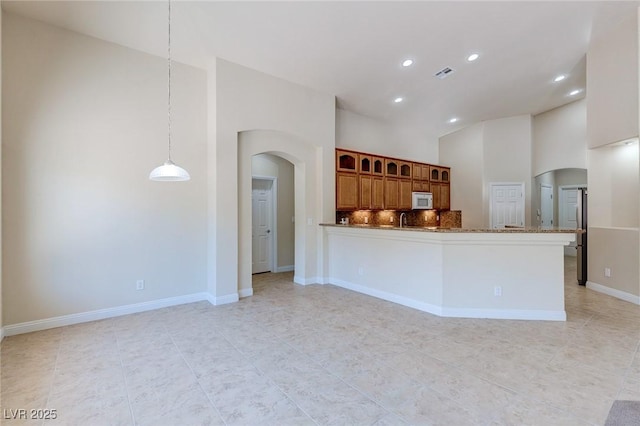 kitchen featuring white microwave, arched walkways, recessed lighting, brown cabinetry, and light tile patterned floors