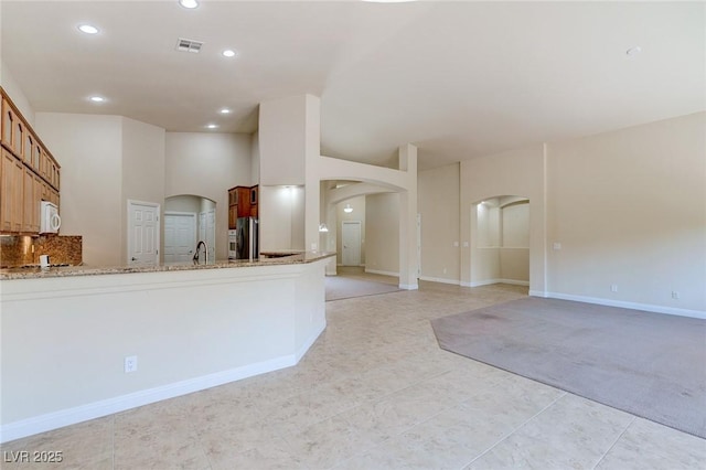 kitchen featuring arched walkways, white microwave, freestanding refrigerator, recessed lighting, and light stone counters