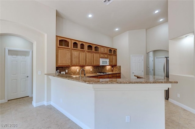 kitchen with white appliances, arched walkways, decorative backsplash, glass insert cabinets, and light stone counters
