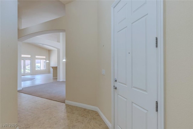 hall featuring arched walkways, carpet, tile patterned floors, and baseboards