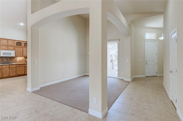 foyer with arched walkways, light tile patterned flooring, light colored carpet, high vaulted ceiling, and baseboards