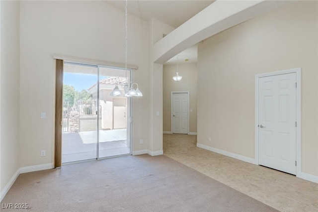 unfurnished dining area with a high ceiling, carpet floors, a chandelier, arched walkways, and baseboards