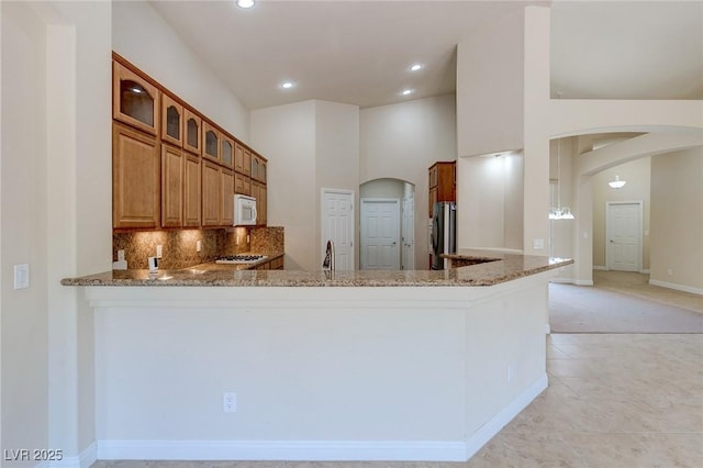 kitchen with arched walkways, white microwave, light stone counters, glass insert cabinets, and recessed lighting