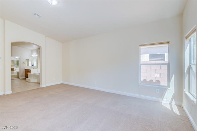 empty room featuring light colored carpet, arched walkways, and baseboards