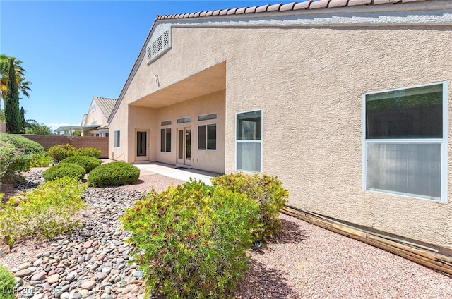 rear view of house with stucco siding, fence, and a patio