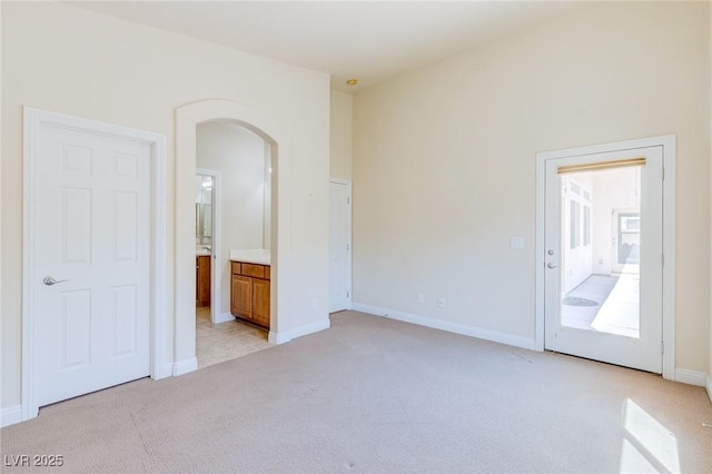 spare room with arched walkways, light carpet, and baseboards