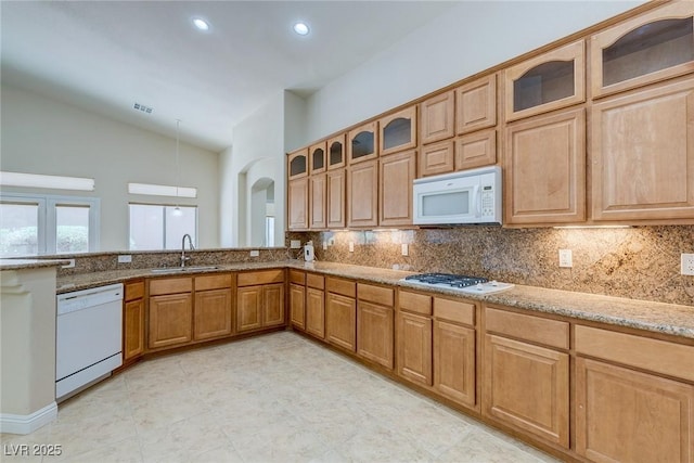 kitchen featuring white appliances, a sink, vaulted ceiling, light stone countertops, and tasteful backsplash
