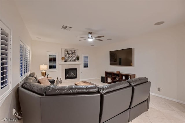 living room featuring ceiling fan, light tile patterned flooring, a tile fireplace, and baseboards