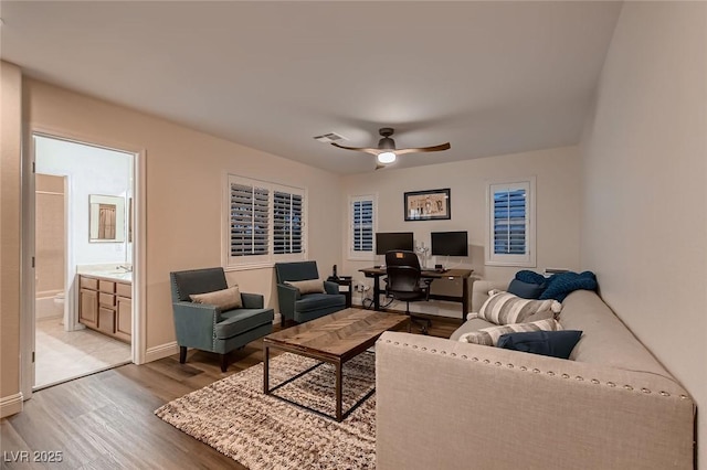 living room with light wood-style flooring, a desk, a ceiling fan, and baseboards