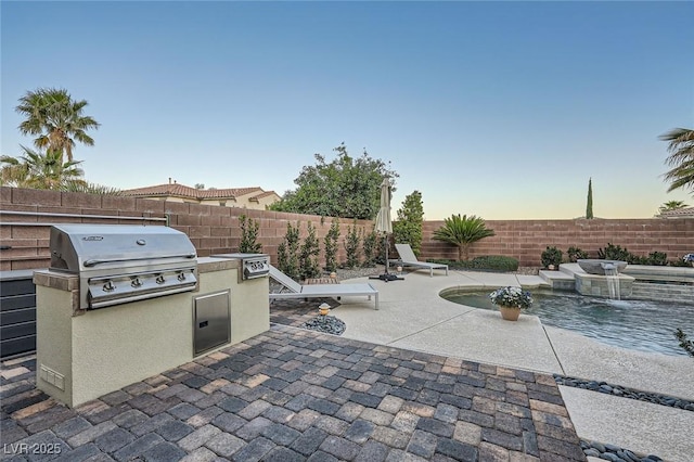 patio terrace at dusk featuring exterior kitchen, area for grilling, and a fenced backyard