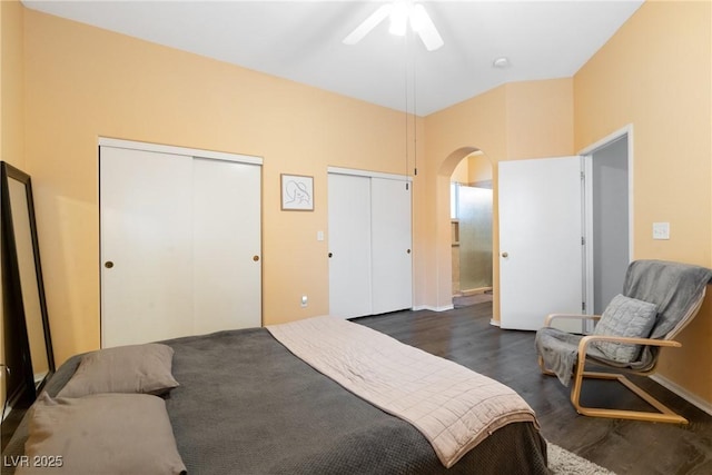 bedroom featuring multiple closets, arched walkways, dark wood-style floors, a ceiling fan, and baseboards