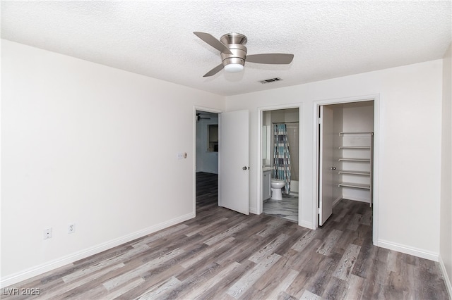 unfurnished bedroom with wood finished floors, a walk in closet, a closet, baseboards, and a textured ceiling