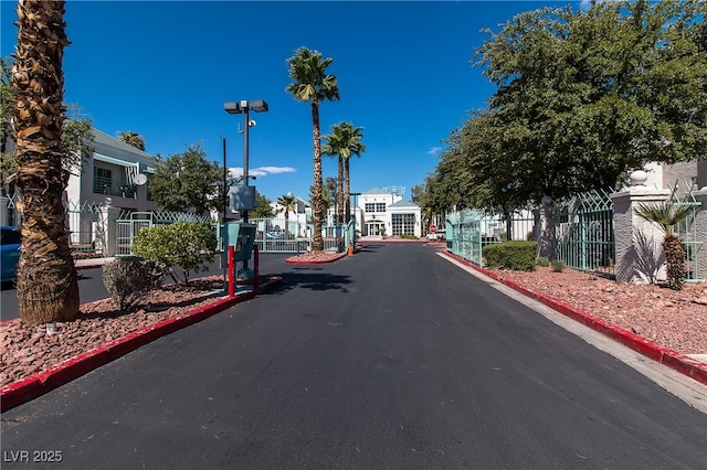 view of asphalt street featuring curbs, a gated entry, street lights, a gate, and a residential view