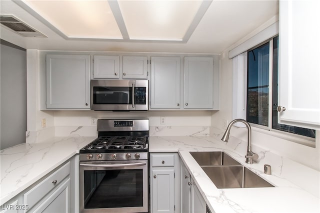kitchen with appliances with stainless steel finishes, a sink, and light stone countertops