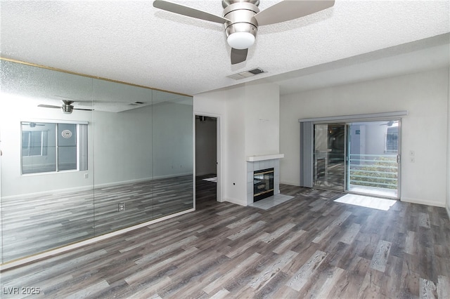 unfurnished living room featuring a ceiling fan, wood finished floors, a textured ceiling, baseboards, and a fireplace