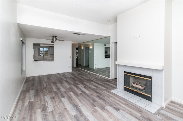 unfurnished living room with wood finished floors, a tiled fireplace, a ceiling fan, and baseboards
