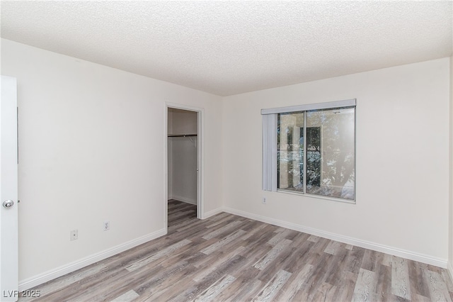 unfurnished bedroom featuring light wood-style flooring, a closet, baseboards, a textured ceiling, and a walk in closet