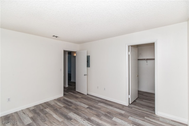 unfurnished bedroom featuring wood finished floors, baseboards, a walk in closet, a closet, and electric panel