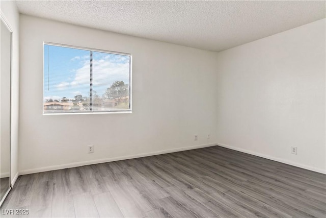 spare room with wood finished floors, a textured ceiling, and baseboards