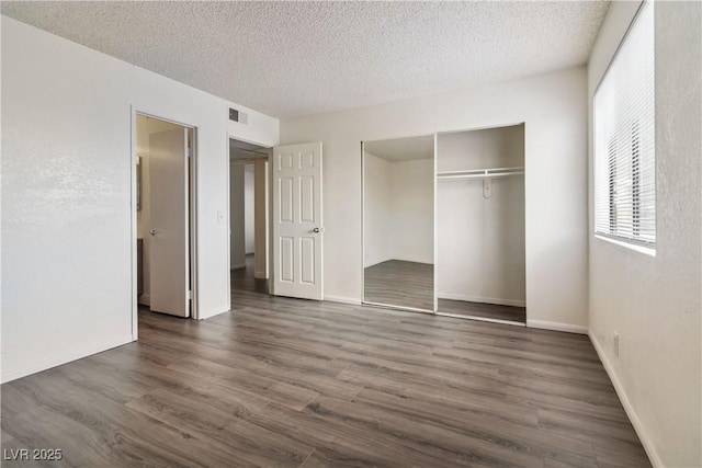 unfurnished bedroom featuring a textured ceiling, dark wood finished floors, a closet, and baseboards