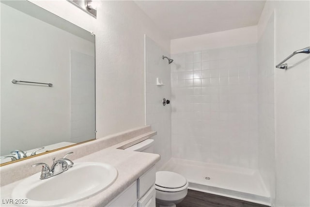 full bathroom featuring toilet, a tile shower, and vanity