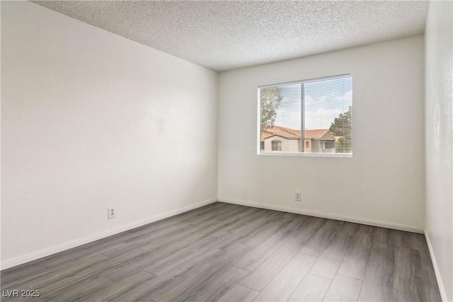 unfurnished room with wood finished floors, a textured ceiling, and baseboards