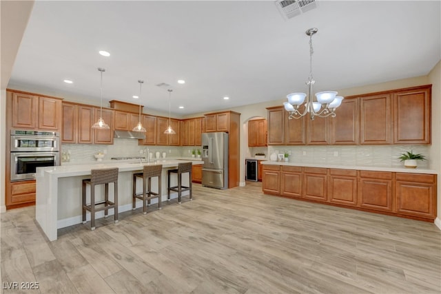 kitchen featuring stainless steel appliances, under cabinet range hood, light countertops, decorative backsplash, and brown cabinets