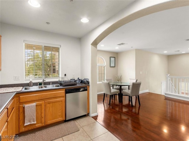 6488 Bentley Wood Ct, Las Vegas, NV 89130 - kitchen with dishwasher, a sink, arched walkways, brown cabinetry, and light tile patterned floors