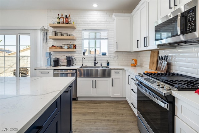 kitchen with stainless steel appliances, white cabinets, a sink, decorative backsplash, and light wood finished floors