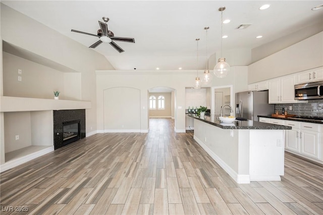 3882 Genoa Dr, Las Vegas, NV 89141 - kitchen featuring stainless steel appliances, arched walkways, light wood-style flooring, open floor plan, and white cabinets