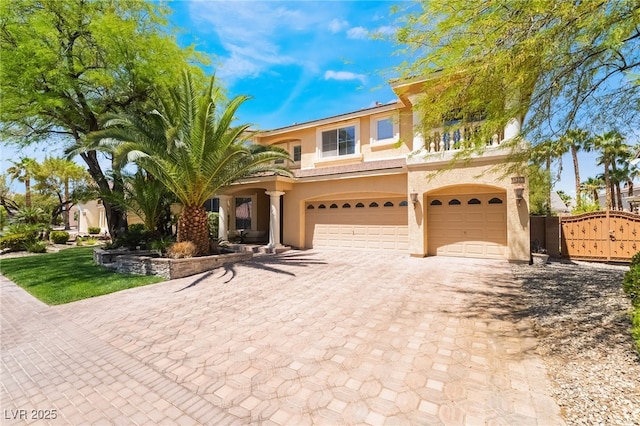 view of front of home with an attached garage, stucco siding, decorative driveway, and a gate