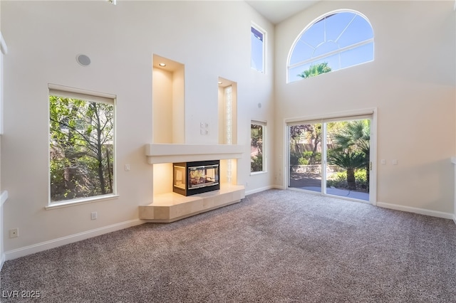 unfurnished living room featuring a towering ceiling, carpet floors, a tiled fireplace, and baseboards