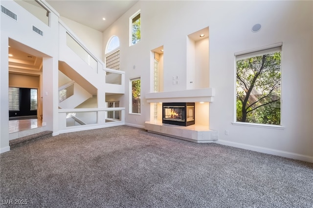 unfurnished living room featuring carpet, plenty of natural light, a high ceiling, a tile fireplace, and baseboards
