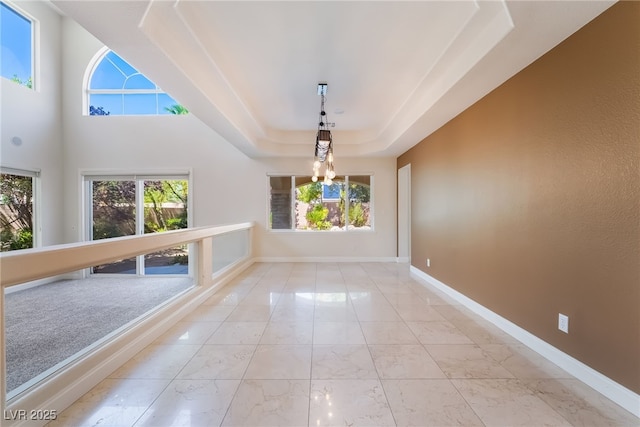 unfurnished dining area featuring a raised ceiling, marble finish flooring, plenty of natural light, and baseboards